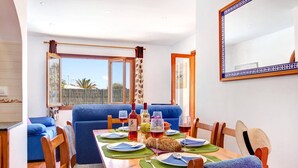 Comedor con una mesa dispuesta para cuatro personas, sillas tapizadas en azul, una mesa de madera y vistas al exterior a través de amplias ventanas.