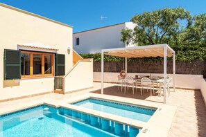 Un espace piscine doté d’un patio couvert, d’une table avec des chaises et d’une petite fenêtre avec des volets.