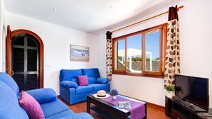 Una sala de estar con un sofá azul, una mesa de centro, un televisor y una ventana con cortinas.