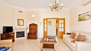A living room with a fireplace, a television, a wooden cabinet, a coffee table, and a white sofa. - Villa Arvela by Villa Plus (Vale Rebelho)