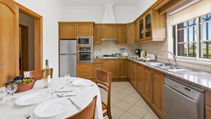 A kitchen with wooden cabinets, a stainless steel refrigerator, an oven, a dishwasher, and a dining table set with plates and cutlery. - Villa Arvela by Villa Plus (Vale Rebelho)