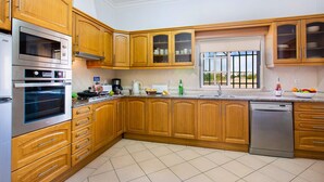 A modern kitchen with wooden cabinets, stainless steel appliances, and a tiled backsplash. - Villa Arvela by Villa Plus (Vale Rebelho)
