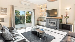 A modern living room with a fireplace, a flat-screen TV, and a sliding glass door leading to a balcony. - Villa Casa do Mel by Villa Plus (Loule)