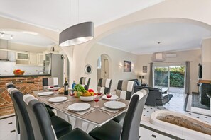 A modern dining area with a brick accent wall, a large table set for six, and a view of the kitchen and outdoor patio.