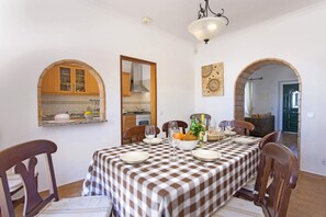 A dining area with a checkered tablecloth, wooden chairs, and a buffet table with fruits and glasses.