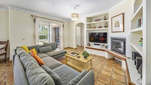 Een woonkamer met een bank, salontafel, televisie, open haard en modelboten op planken.