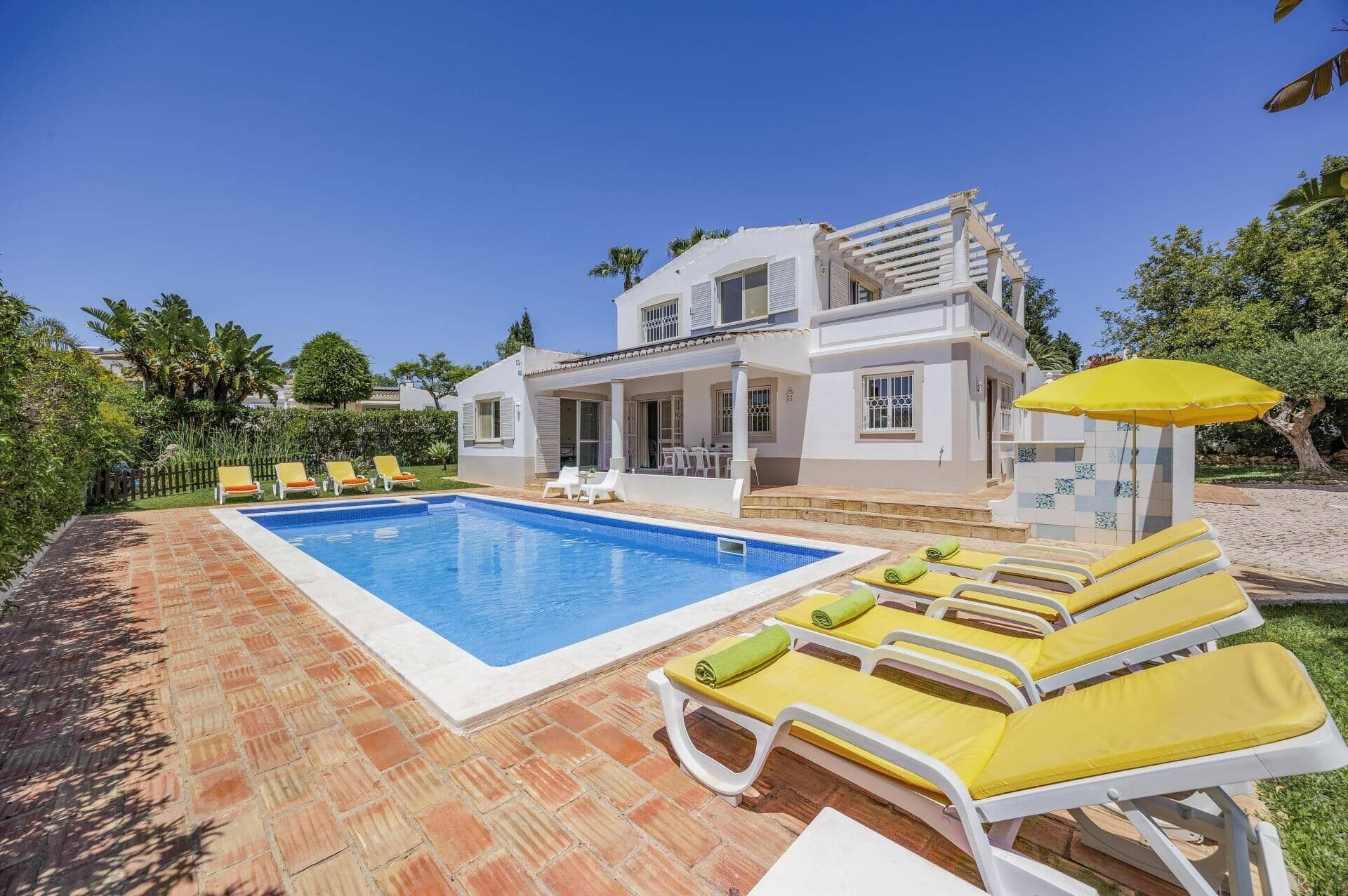 A two-story house with a swimming pool, sun loungers, and a covered patio area.