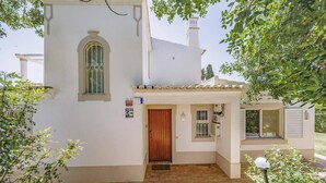 Un bâtiment blanc avec une porte en bois, une fenêtre grillagée et un petit porche.