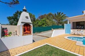 Un patio con chimenea de ladrillo, piscina y mobiliario exterior.