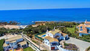 Una villa costiera con vista sul mare, circondata da vegetazione e altri edifici.