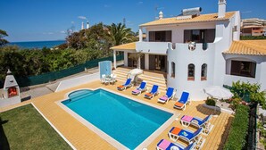 Una grande piscina con lettini e ombrelloni, circondata da un prato curato e vista sul mare.