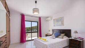 Camera da letto con un letto, comodini, una cassettiera, una finestra con tende, una lampada a soffitto e vista su alberi.