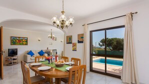 Zona pranzo con tavolo imbandito per quattro persone, un lampadario e vista su una piscina attraverso un'ampia porta scorrevole in vetro.