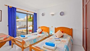 A bedroom with two wooden beds, a small table, a chair, and a sliding glass door leading to a balcony. - Villa Lisson Grove by Villa Plus (Carvoeiro)