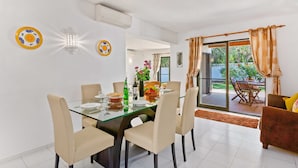 A dining area with a glass table and chairs, a buffet table with food and drinks, and a view of a garden through a sliding glass door. - Villa Lisson Grove by Villa Plus (Carvoeiro)