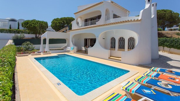 Uma vila branca de dois andares com piscina e área de estar externa.