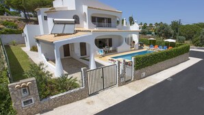 Uma villa moderna e branca com piscina, área de estar externa e um muro de pedra.