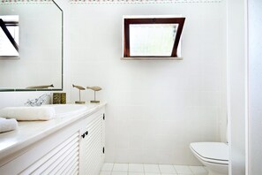 Une salle de bain avec un meuble-lavabo blanc, un miroir, une petite fenêtre et des toilettes.