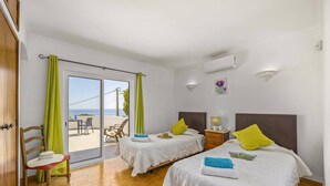 Quarto de hotel com duas camas, varanda com vista, piso de madeira e parede branca.