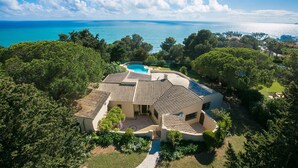 Eine mediterrane Villa mit Swimmingpool, umgeben von üppiger Vegetation und Blick auf das klare, blaue Meer.