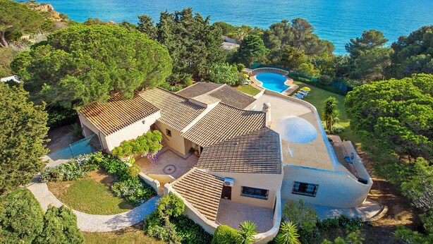 Eine Villa mit Swimmingpool, umgeben von üppiger Vegetation und Blick auf das klare, blaue Meer.