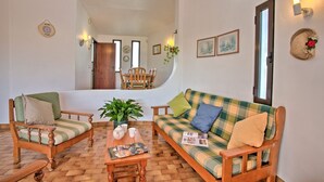 Una sala de estar acogedora con un sofá, dos sillones, una mesa de centro y un comedor al fondo.