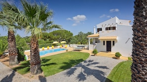 Eine weiße Villa mit Swimmingpool, Palmen und einer gepflasterten Terrasse.