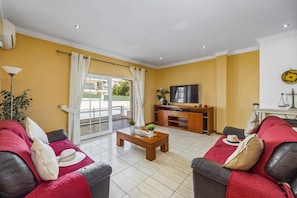 A living room with a TV, sofa, coffee table, and a view of a pool through a sliding glass door.