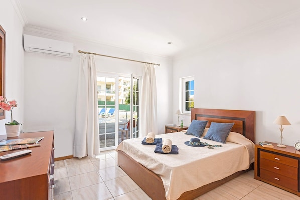 A hotel room with a bed, bedside table, lamp, and a view of the outside. - Villa Carvalho by Villa Plus (Albufeira)