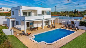 Ett modernt hus i två våningar med en swimmingpool, en uteplats och ett område för grillning.