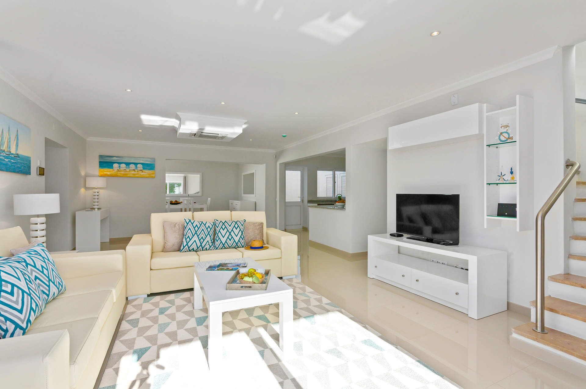 A modern living room with a sofa, coffee table, TV, and a staircase.