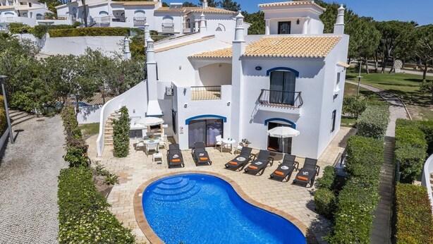 Ein weißes Gebäude mit Swimmingpool, Liegestühlen und einer kleinen Terrasse.