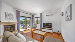 Ein Wohnzimmer mit Sofa, Fernseher, Kamin und Blick ins Freie.