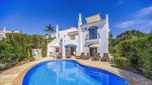 Eine weiße Villa mit Swimmingpool, Außenbereich zum Sitzen und blauem Himmel.