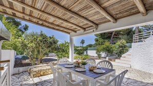 A covered outdoor dining area with a stone floor, white plastic chairs, and a table set for two. - Villa Sawadi by Villa Plus (Praia do Carvoeiro)