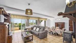 A spacious living area with a sofa, coffee table, dining table with chairs, and a cabinet. - Villa Sawadi by Villa Plus (Praia do Carvoeiro)