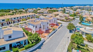 Ett flygbildsbild av ett bostadsområde vid kusten med villor, inklusive Villa Susana, som har tak av terrakotta, frodig grönska och en fri utsikt över havet.