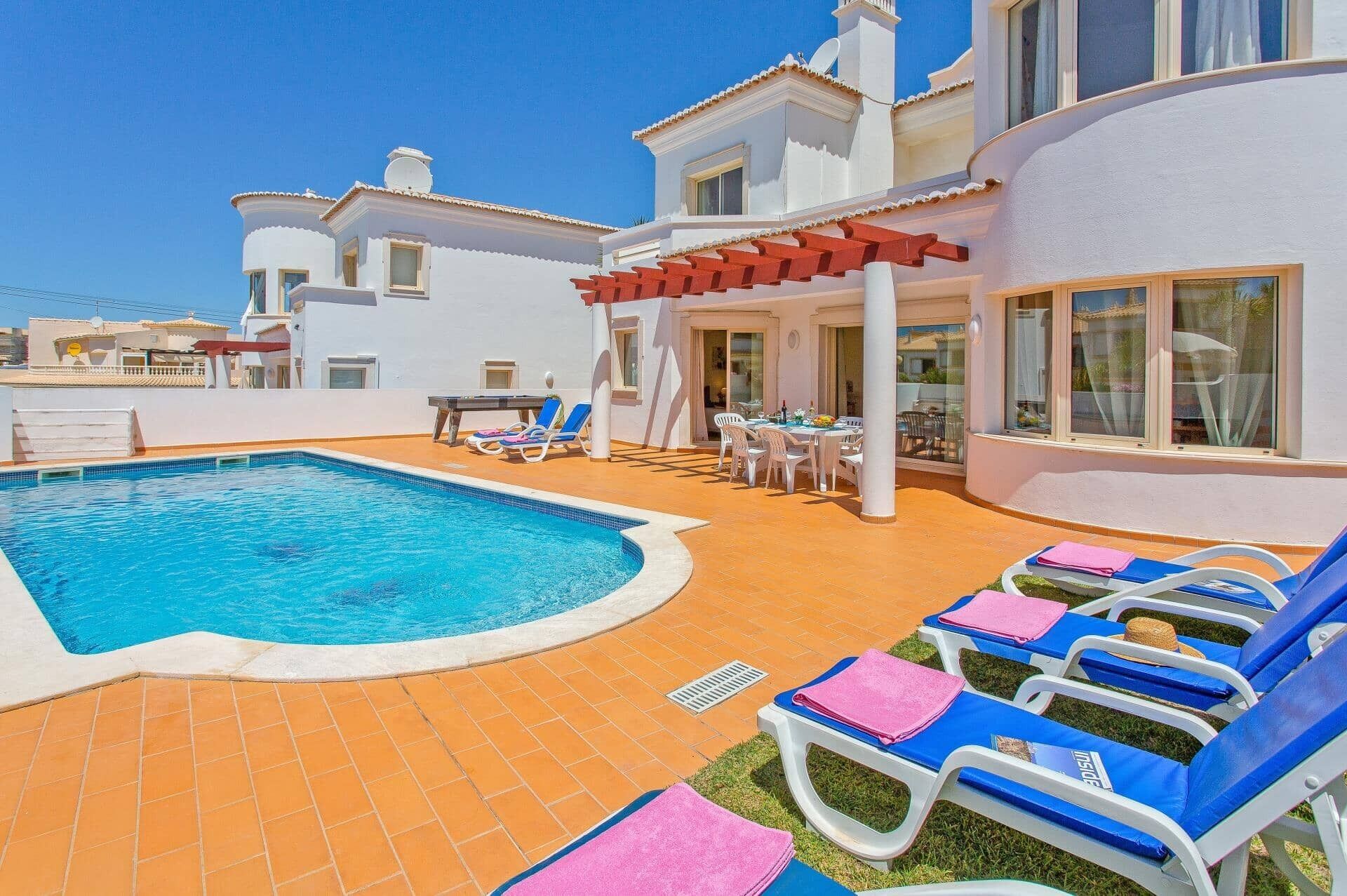 A pool area with lounge chairs and a table, surrounded by a white building with large windows.