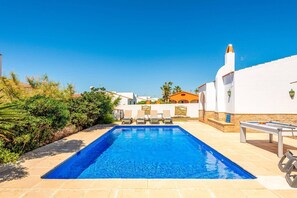 A swimming pool with lounge chairs and a billiards table, surrounded by white buildings and greenery. - Villa Belafranc by Villa Plus (Cap d'Artrutx)