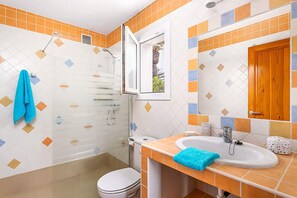 A bathroom with a shower, toilet, sink, and a mirror with a wooden door. - Villa Beltran by Villa Plus (S'Algar)