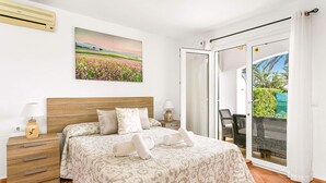 Een slaapkamer met een bed, nachtkastje, lamp, schilderij en een schuifdeur naar een balkon.