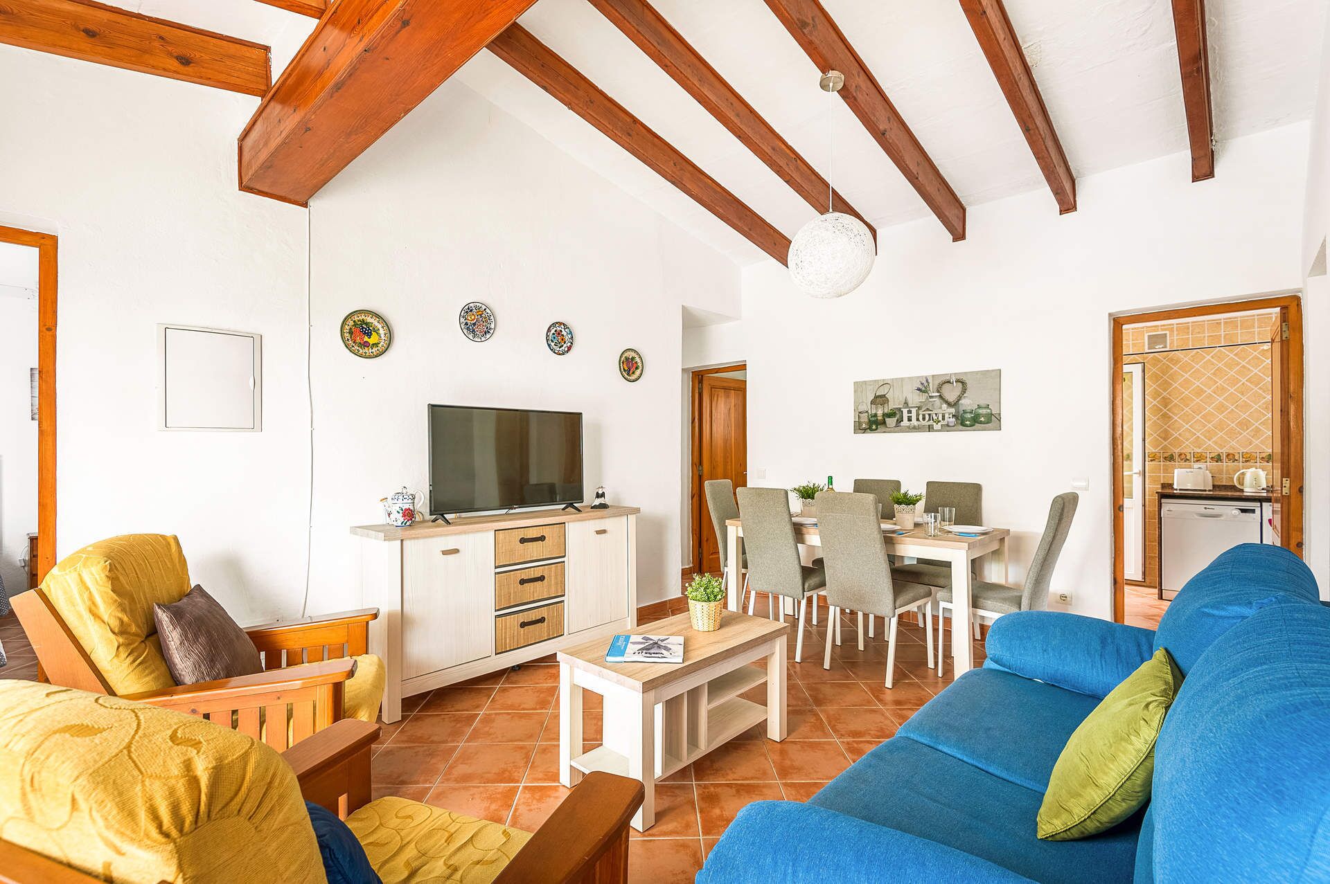 Uma sala de estar com TV, sofá, poltronas e um espaço de refeições com mesa e cadeiras.
