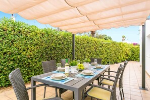 An outdoor dining area with a table set for four, surrounded by wicker chairs with cushions. - Villa Beltran by Villa Plus (S'Algar)