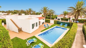Een moderne villa met een zwembad, ligbedden en een trap naar de bovenverdieping.