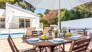 An outdoor dining area with a pool and a table set for two, surrounded by chairs and an umbrella. - Villa Casa Feliz by Villa Plus (Son Parc)