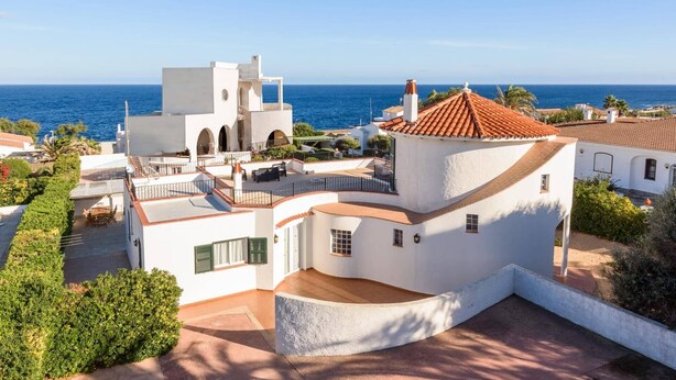 A coastal property with a curved white building, a red-tiled roof, and a view of the sea.