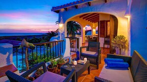 A balcony with wicker furniture, potted plants, and a view of the ocean at sunset. - Villa Corina by Villa Plus (Alayor)