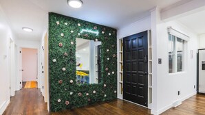 Un pasillo con un muro cubierto de flores verdes, una puerta negra y un espejo.