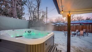 Un jacuzzi con terraza de madera y sillas, rodeado por un patio cubierto de nieve.