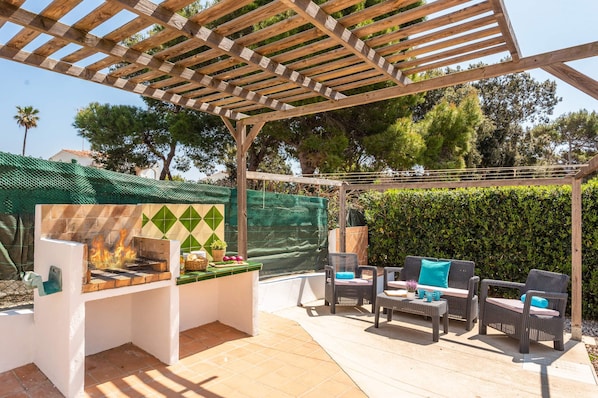 An outdoor patio with a grill, wicker furniture, and a pergola.